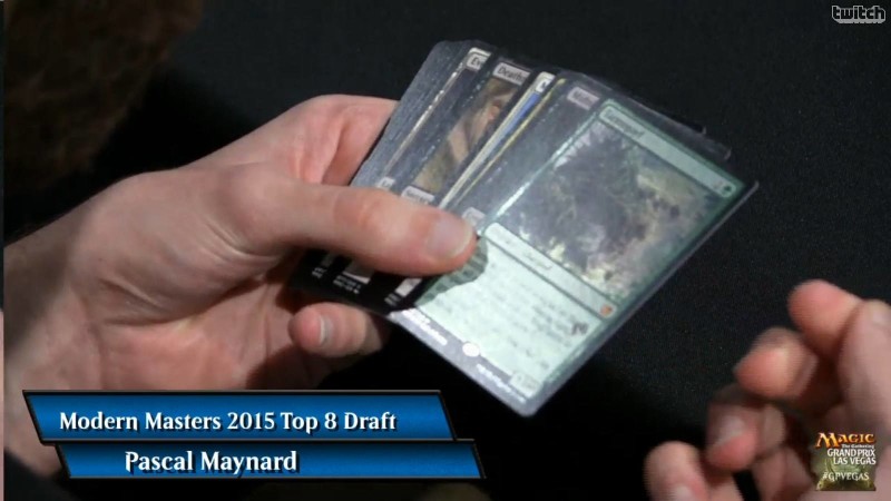 A hand showing a pack of Magic cards in a draft. The front card is a foil Tarmogoyf. This image is from a famous tournament where Maynard opened the incredibly valuable card in their first pack. They decided to keep the card and later sold it for charity.
