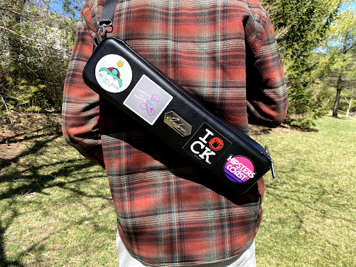 A narrow black Magic case slung across his back, decorated with a line of stickers.