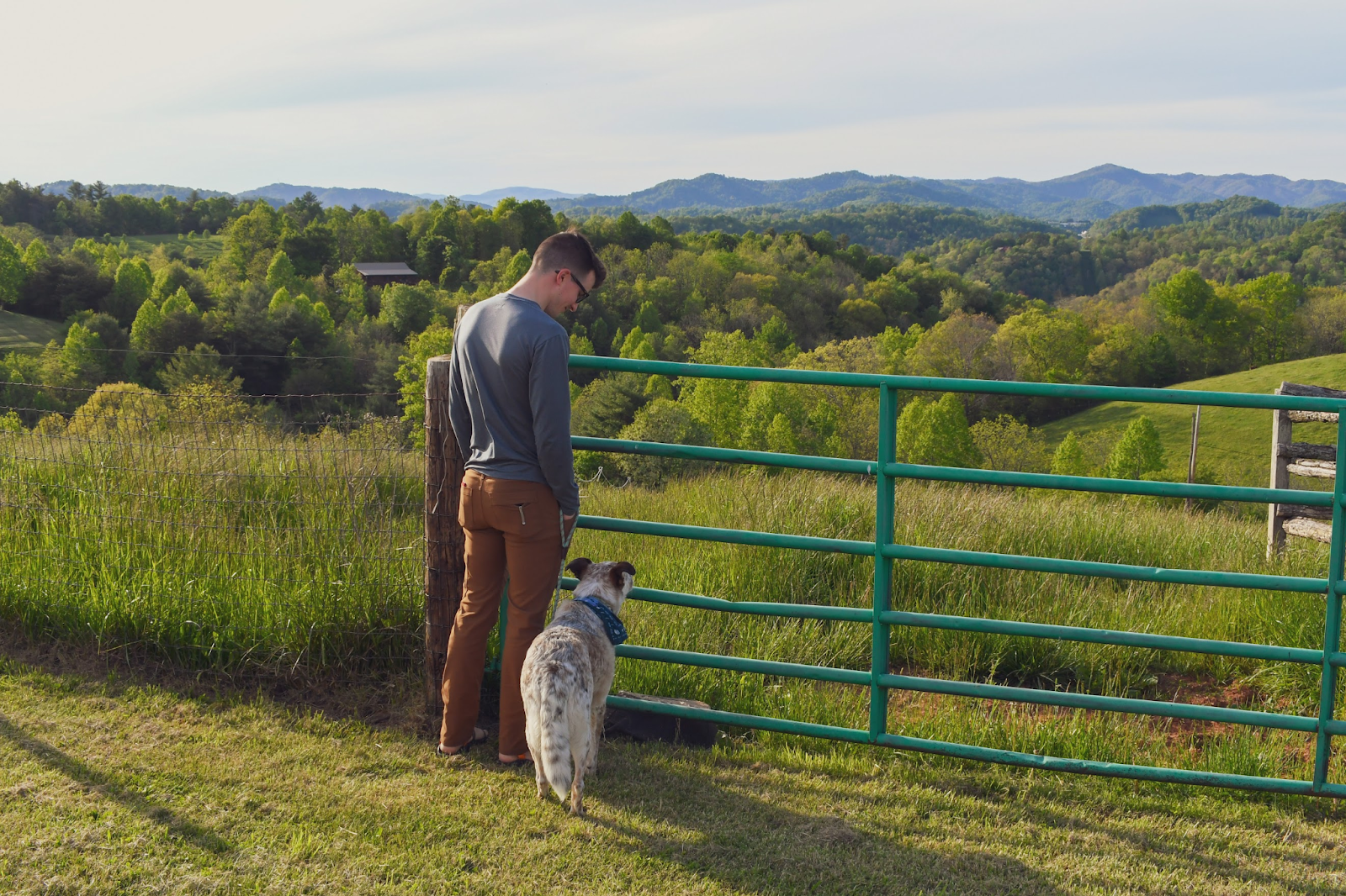 Travis and his dog standing by a green fence overlooking hills.