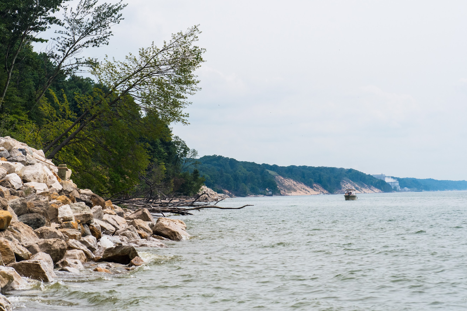 Rocky lake shoreline with forests and boat in the distance.