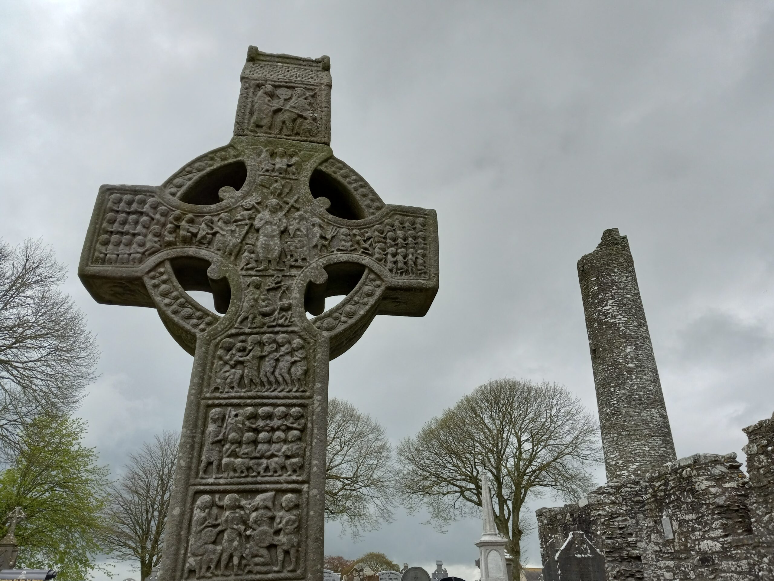 Elements of Monasterboice: Muiredach's High Cross, round tower, stone church walls, modern grave markers. Photograph by the author.