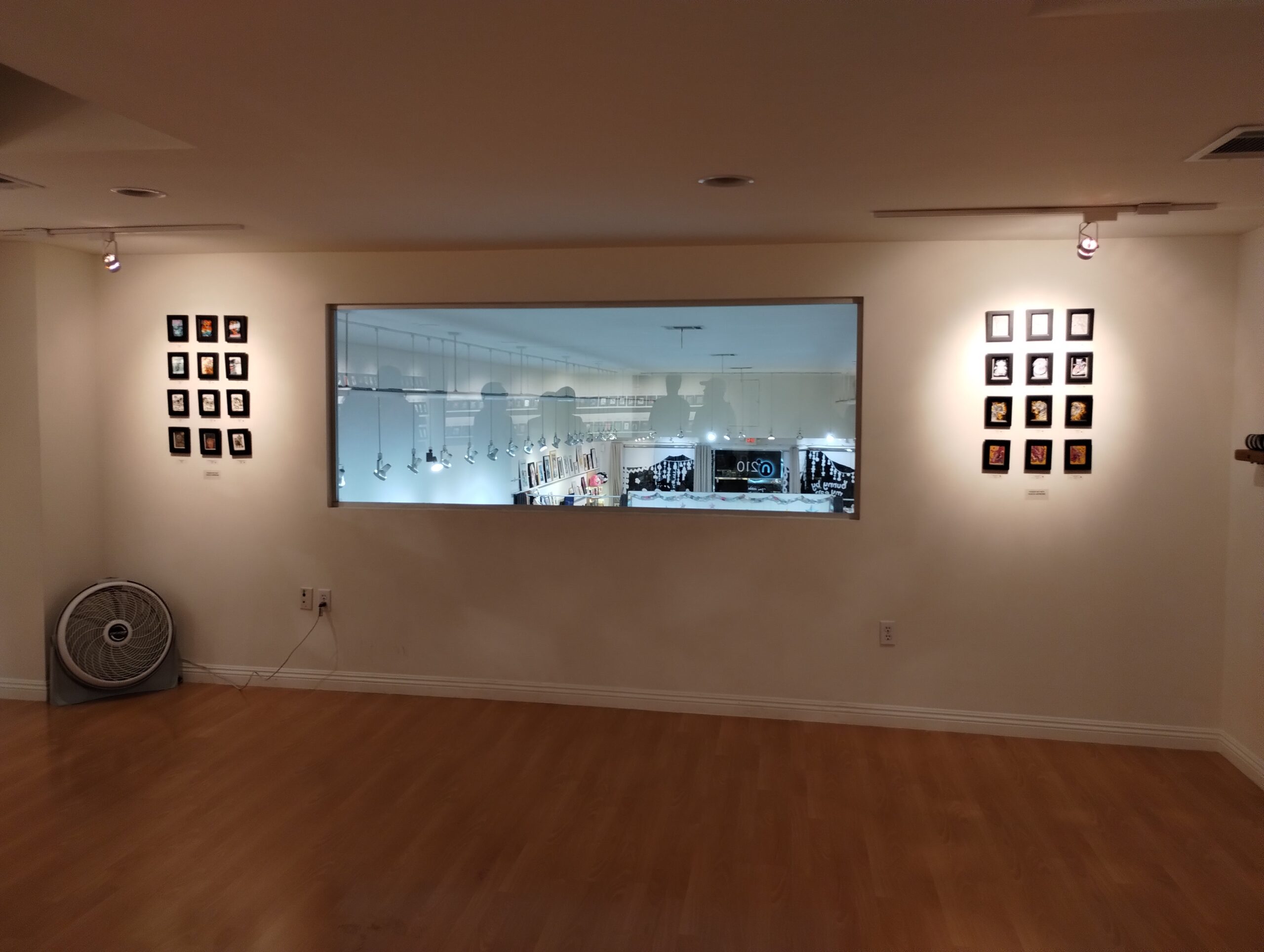 An indoor art gallery with a two sets of miniature paintings framed in a 4x3 grid