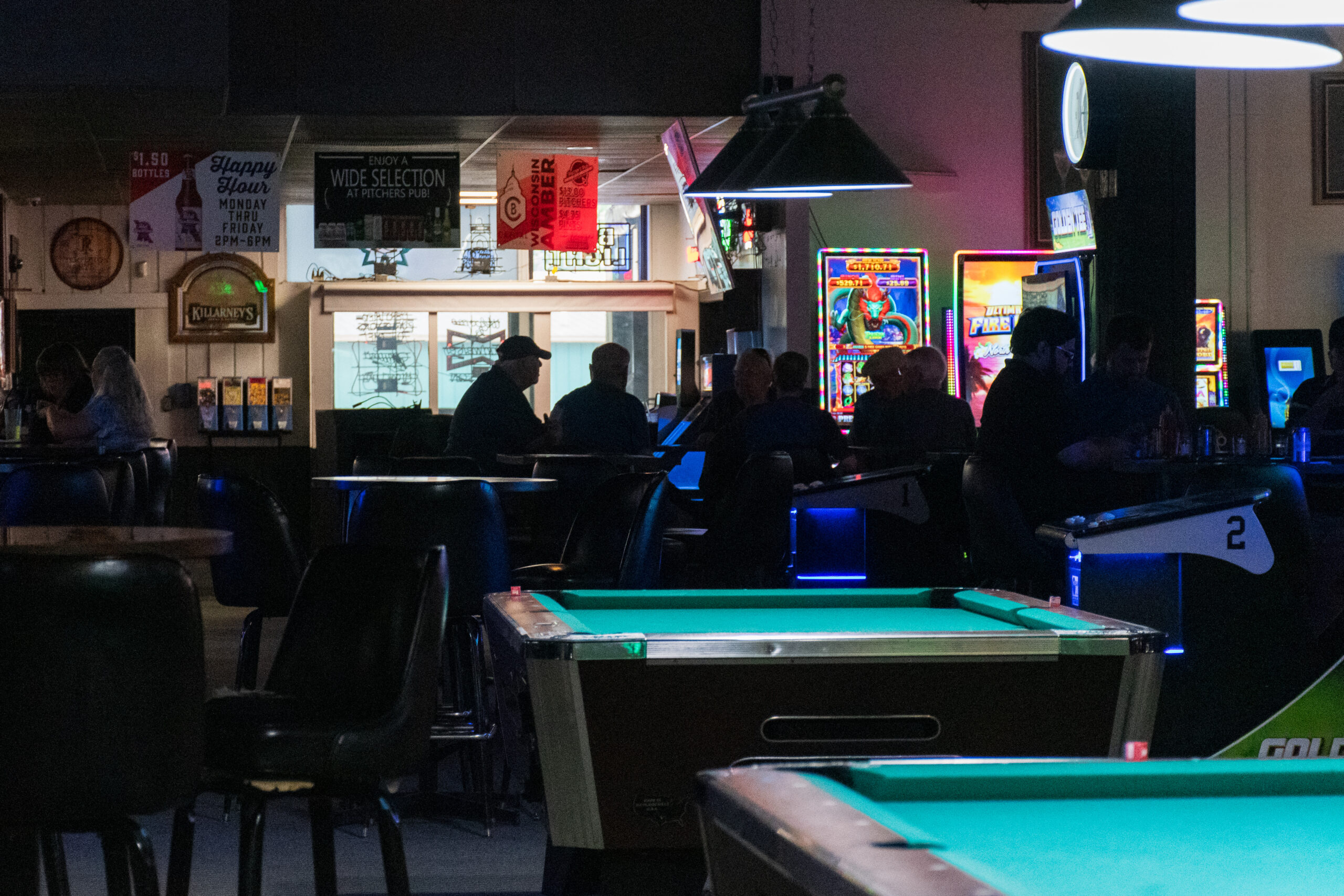 A dimly lit bar with pool tables lit in the foreground