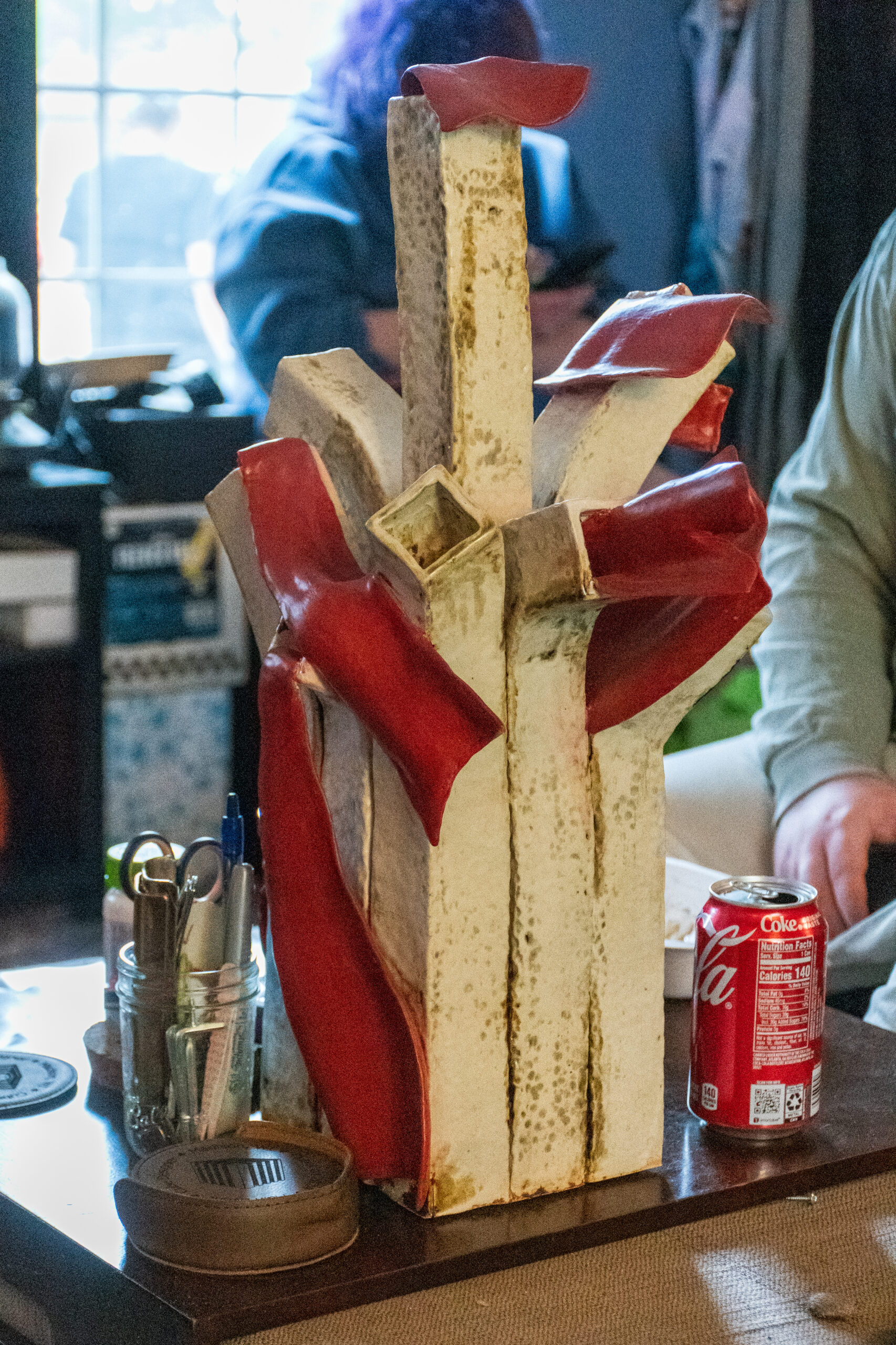 A metal sculpture consisting of white columns and red flag-like elements protruding from it