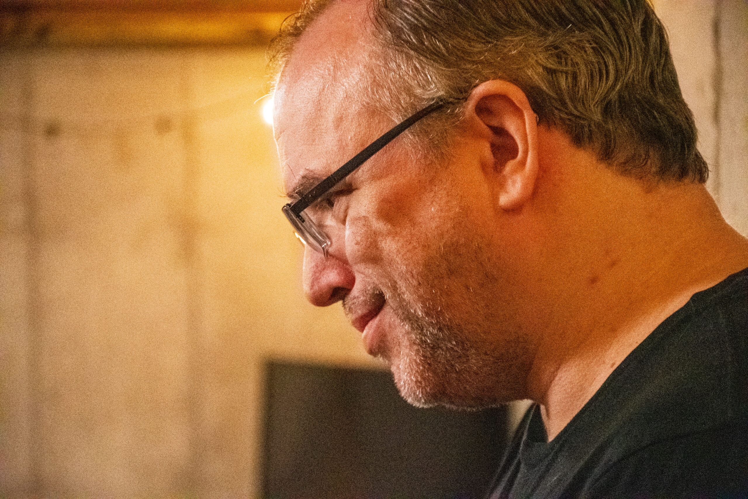 A smiling white man with salt and pepper hair and dark-rimmed glasses, looking off frame