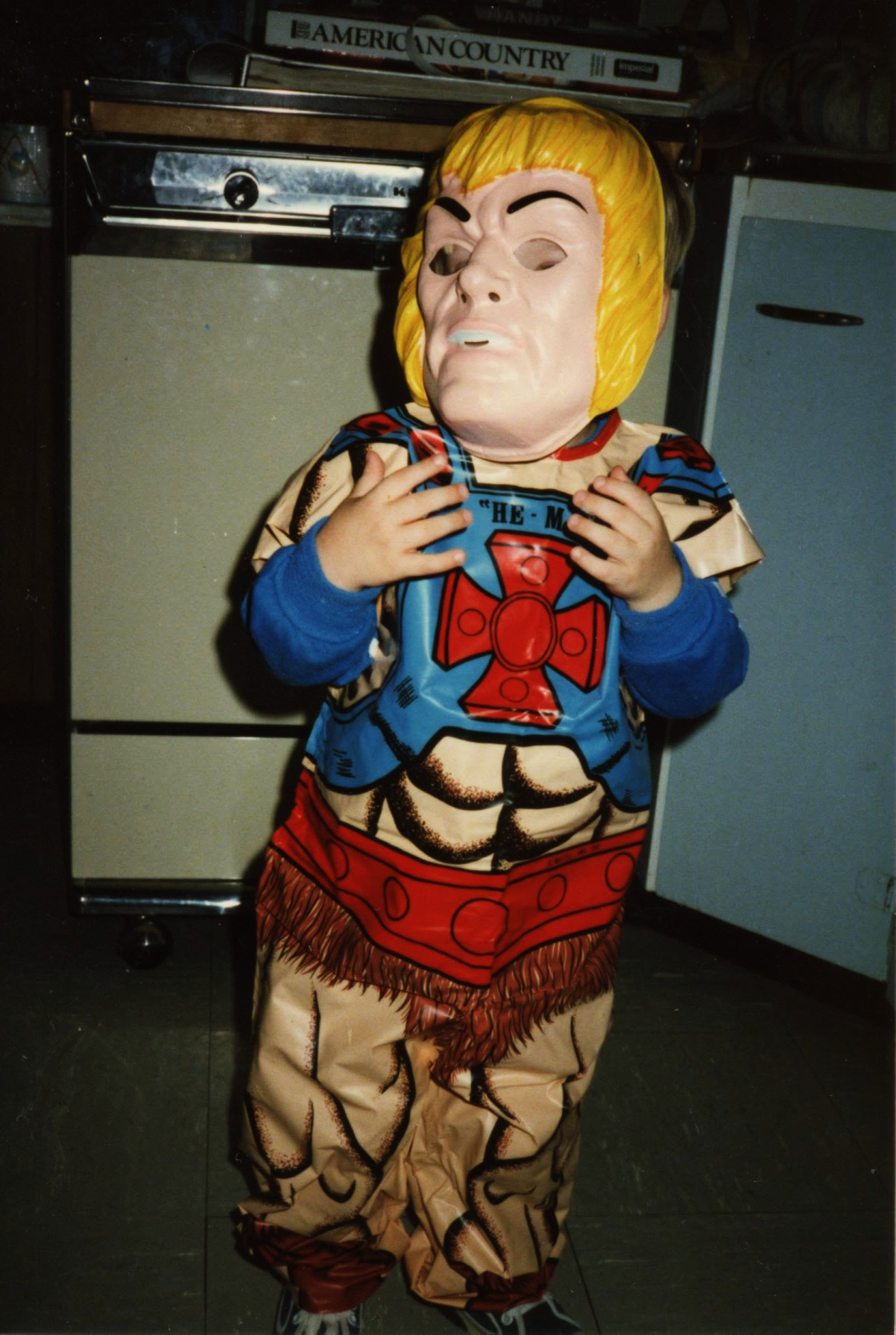 A small child wearing an ill-fitting He-man costume, in a 1980's photograph